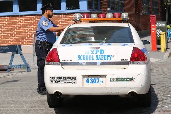 An NYPD school safety officer stands by a squad car.